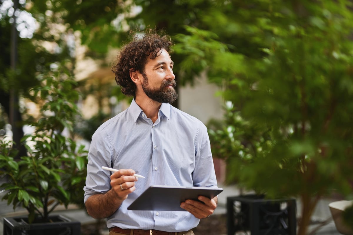 Mid adult businessman using digital tablet outdoors, working remotely and enjoying modern technology