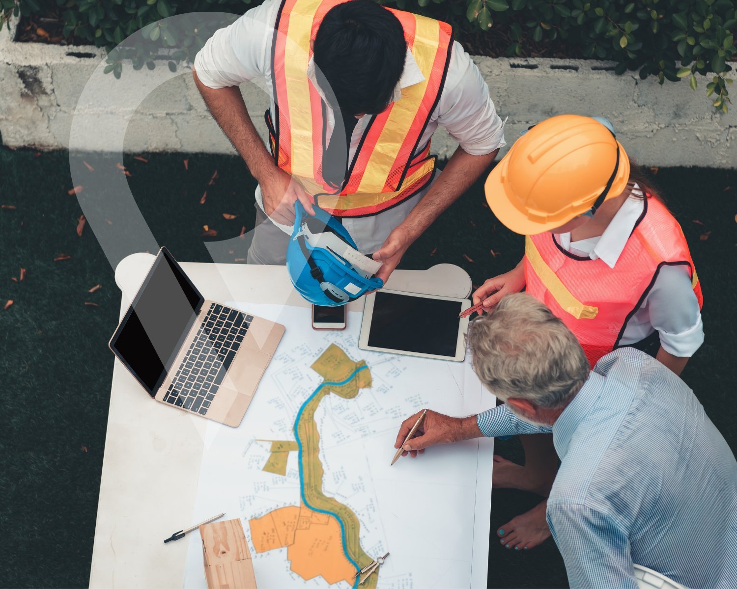 Three construction workers in safety gear reviewing a blueprint and survey map on a table outdoors